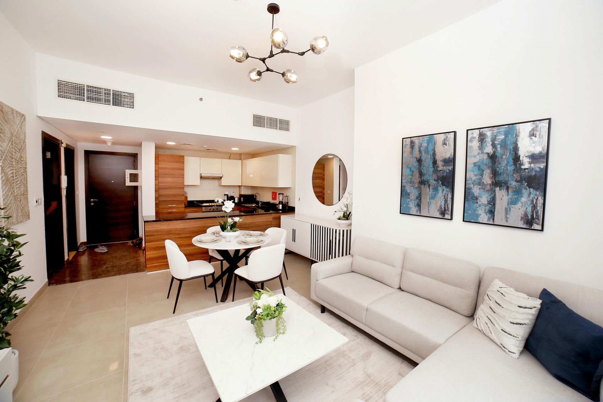 A living room with a couch , table and chairs and a kitchen in the background. FURNITURE ARRANGEMENT