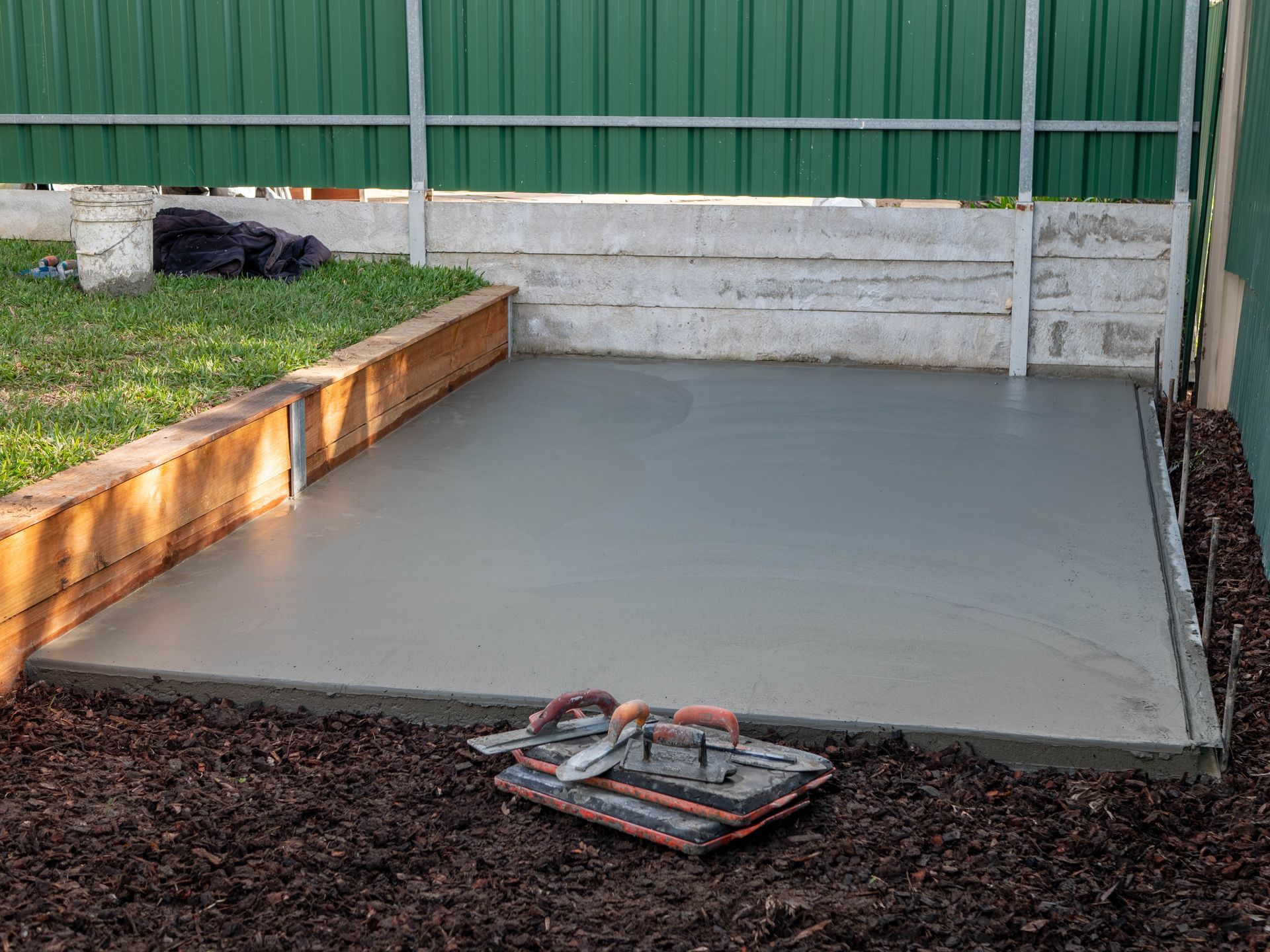 A concrete floor is being built in a backyard next to a green fence.
