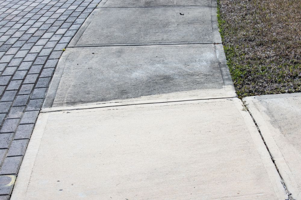 A concrete walkway with a curb and bushes on the side.