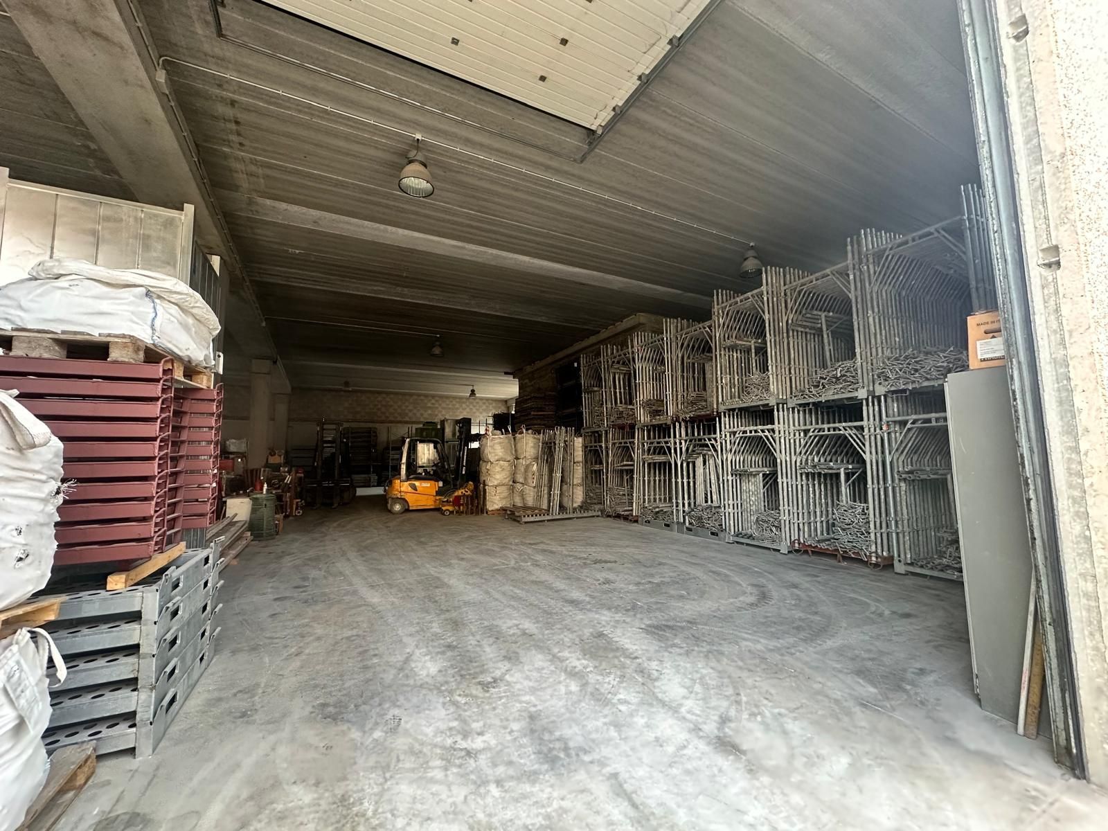 Una veduta grandangolare dell'interno di un magazzino pieno di pile di recinzioni metalliche e un piccolo carrello elevatore parcheggiato in lontananza.