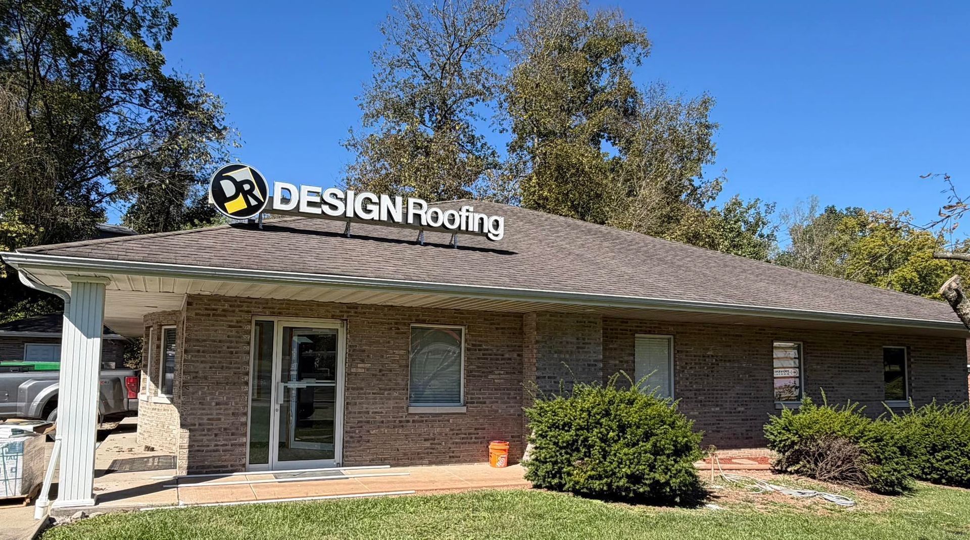 A tan brick building with a brown shingled roof features a sign reading