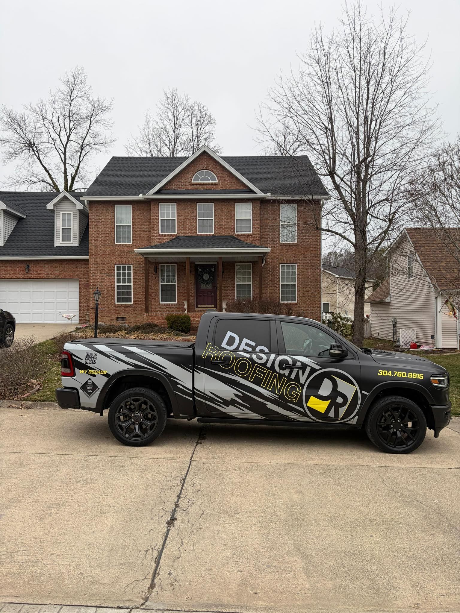 A black pickup truck with grey and yellow geometric decals parked in front of a two-story red brick house.