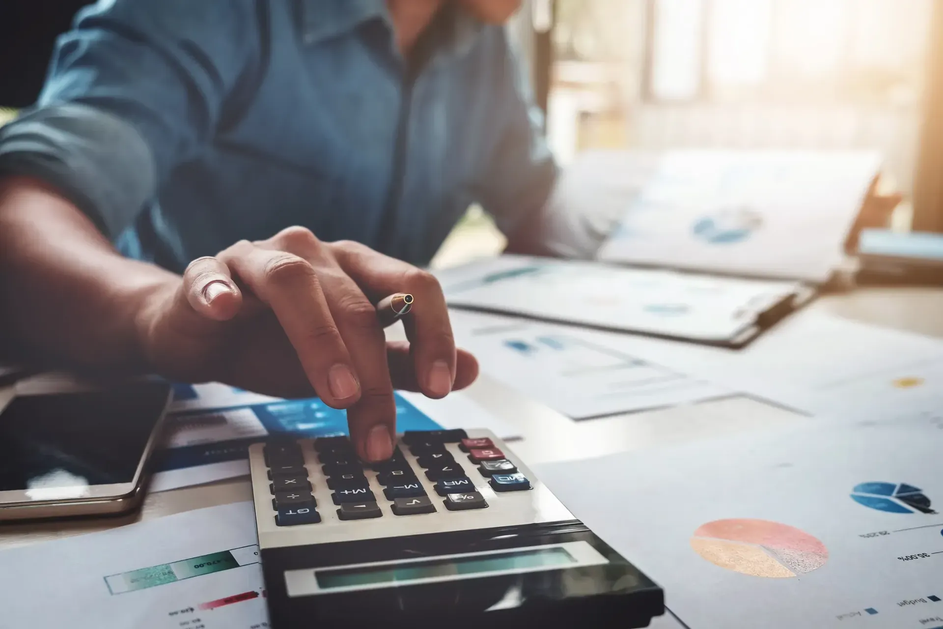 A person using a calculator at a desk with financial charts and documents.