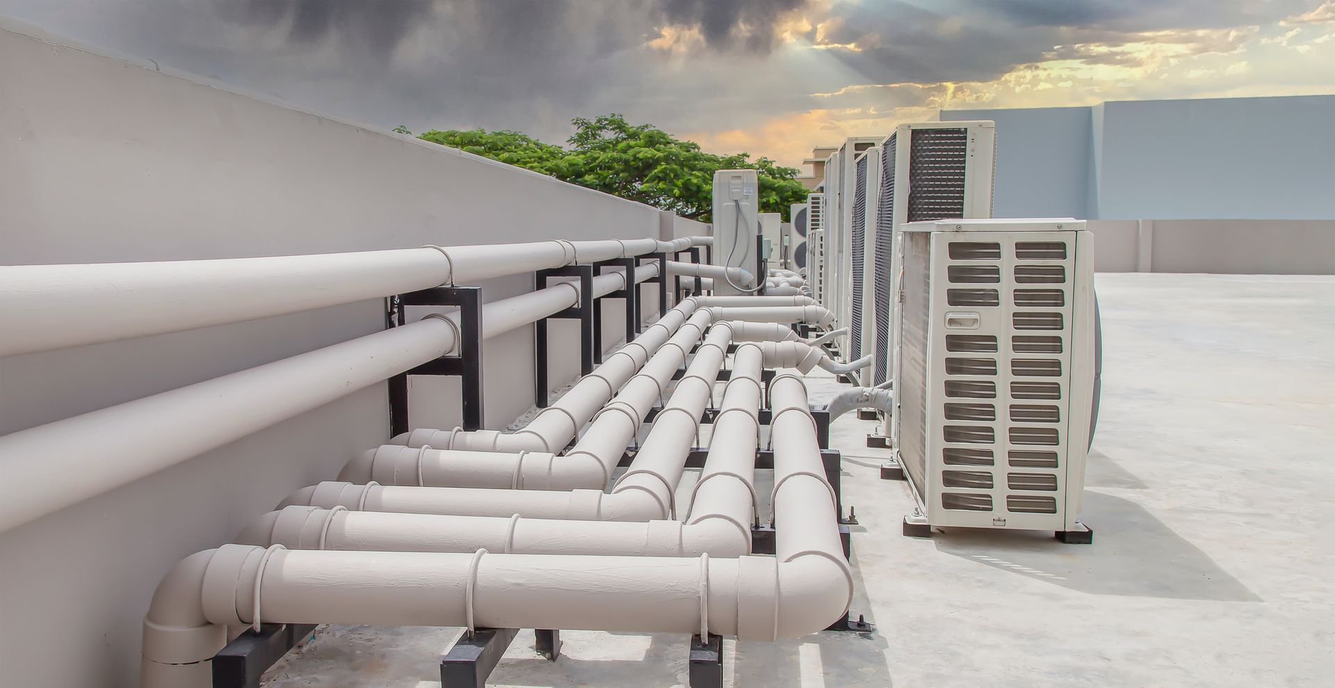 A row of white pipes and air conditioners on the roof of a building.