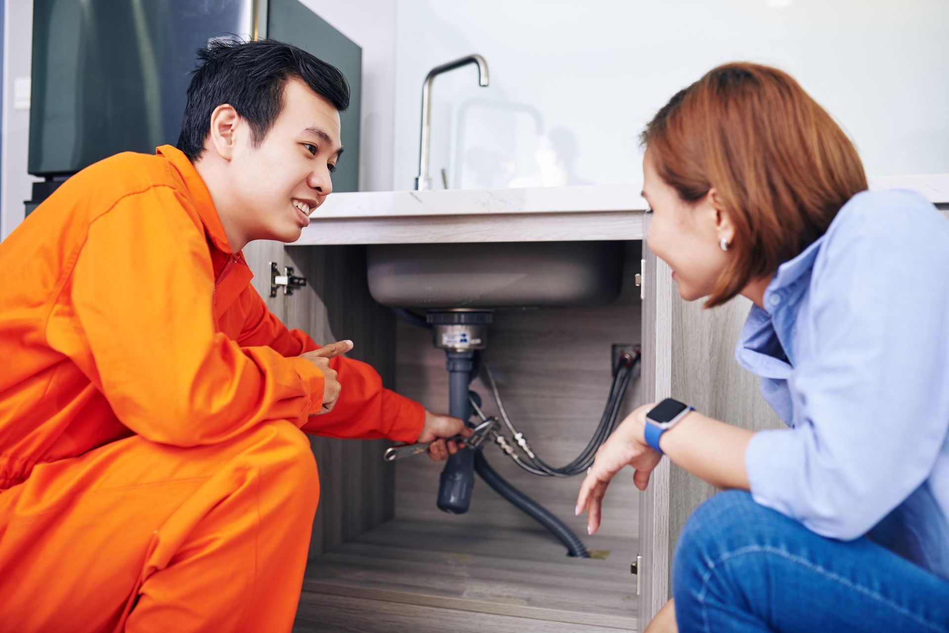 A man and a woman are looking under a sink.