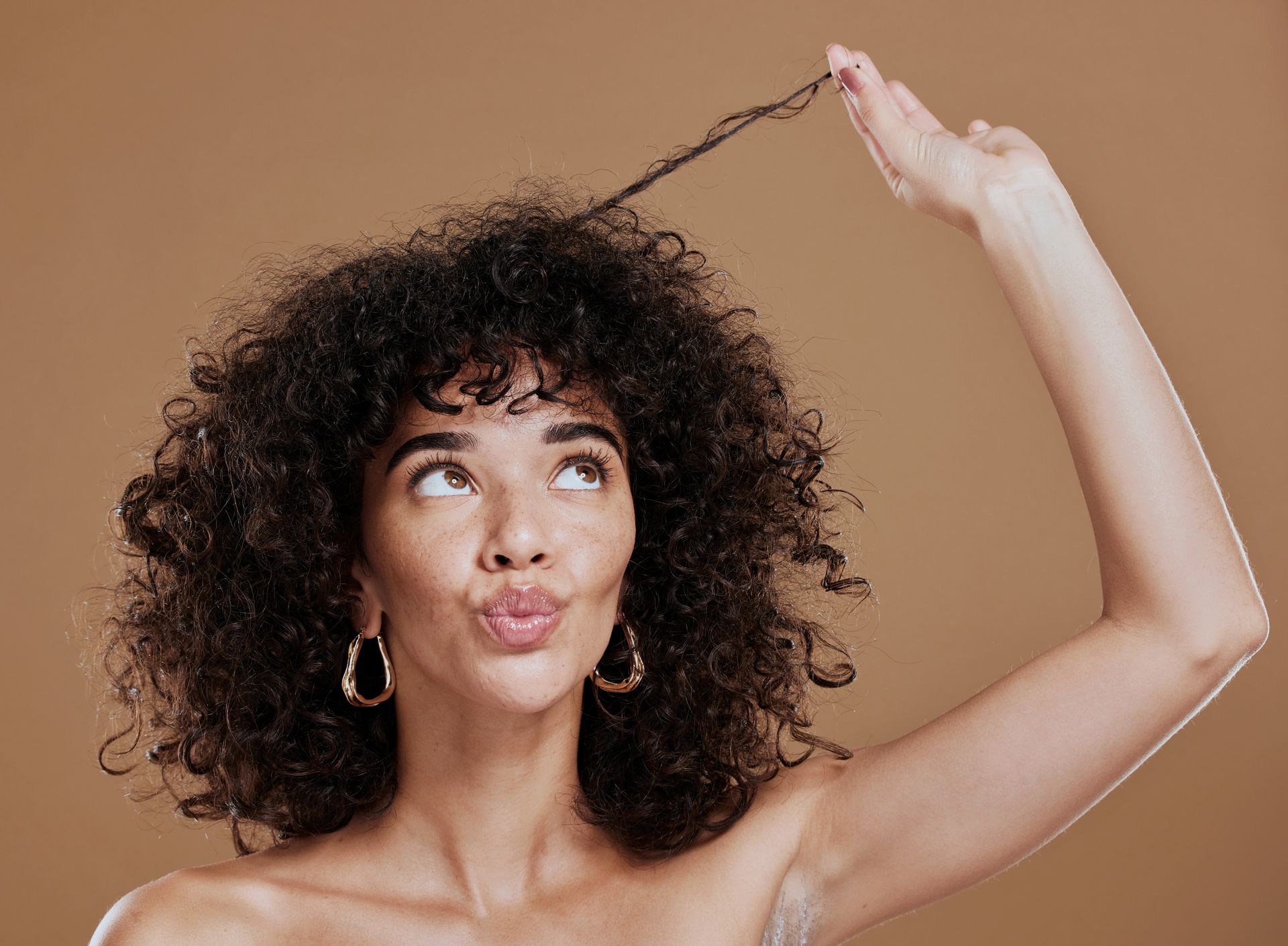 A woman with curly hair is holding her hair in her hand and making a funny face.