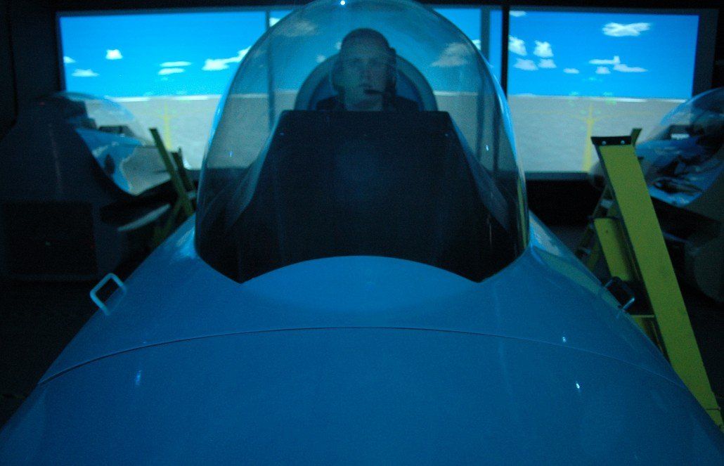 Head on view of customer in f-16 fighter jet flight simulator with screen in background