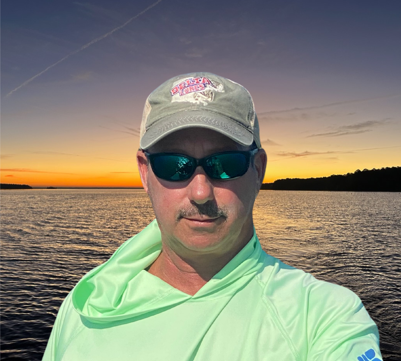 a man wearing sunglasses and a hat is standing in front of a body of water .