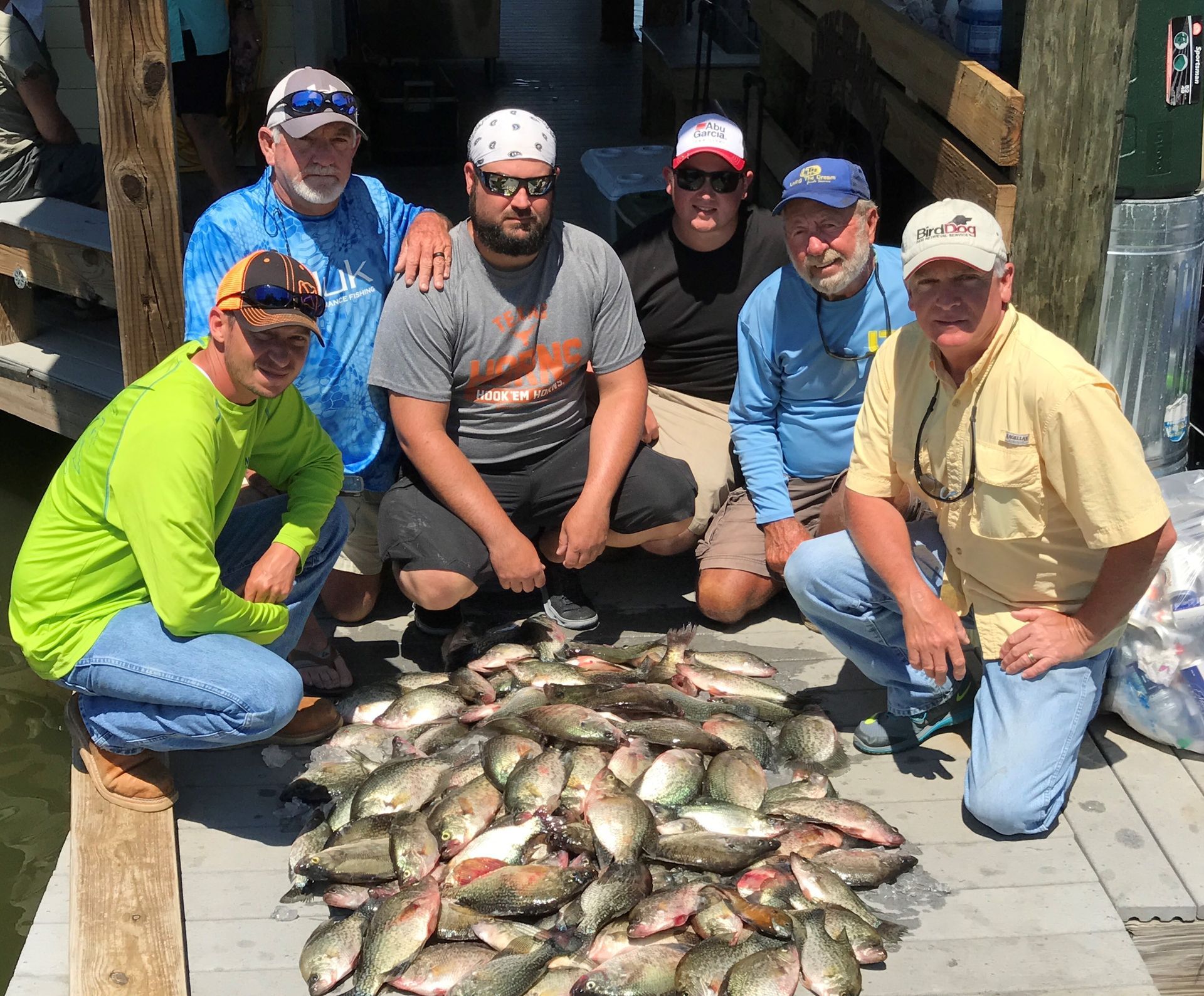 a group of men are posing for a picture with a pile of fish .