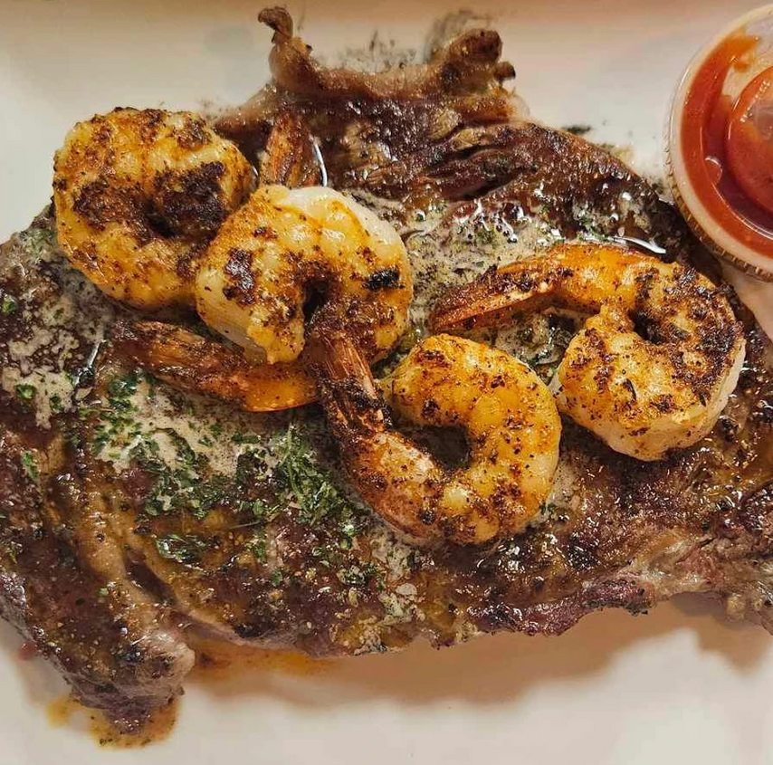 a steak with shrimp and ketchup on a white plate .