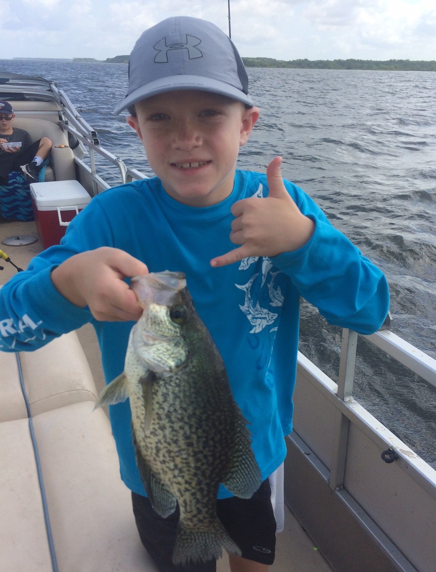 a young boy is holding a fish on a boat and giving a thumbs up