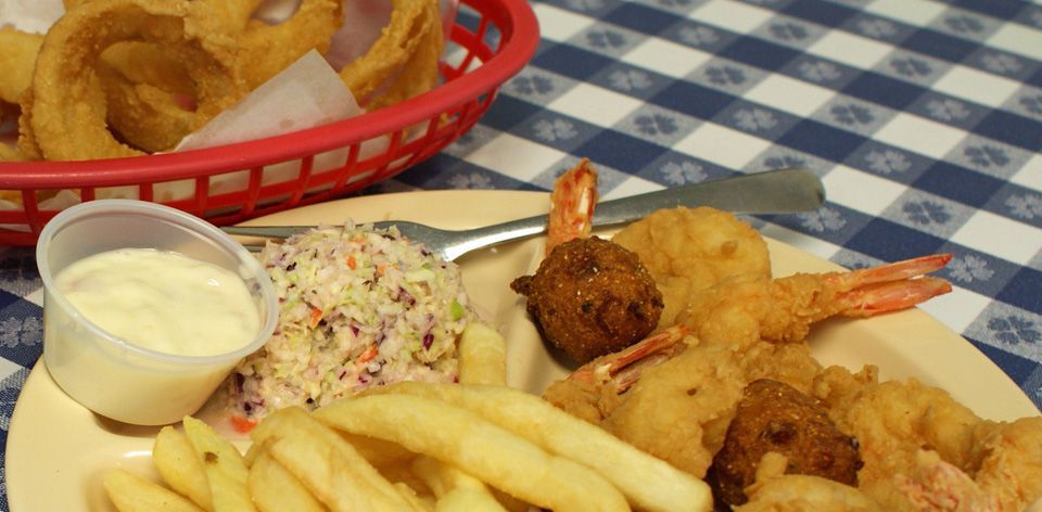 a plate of food with shrimp , french fries , coleslaw and onion rings on a table .