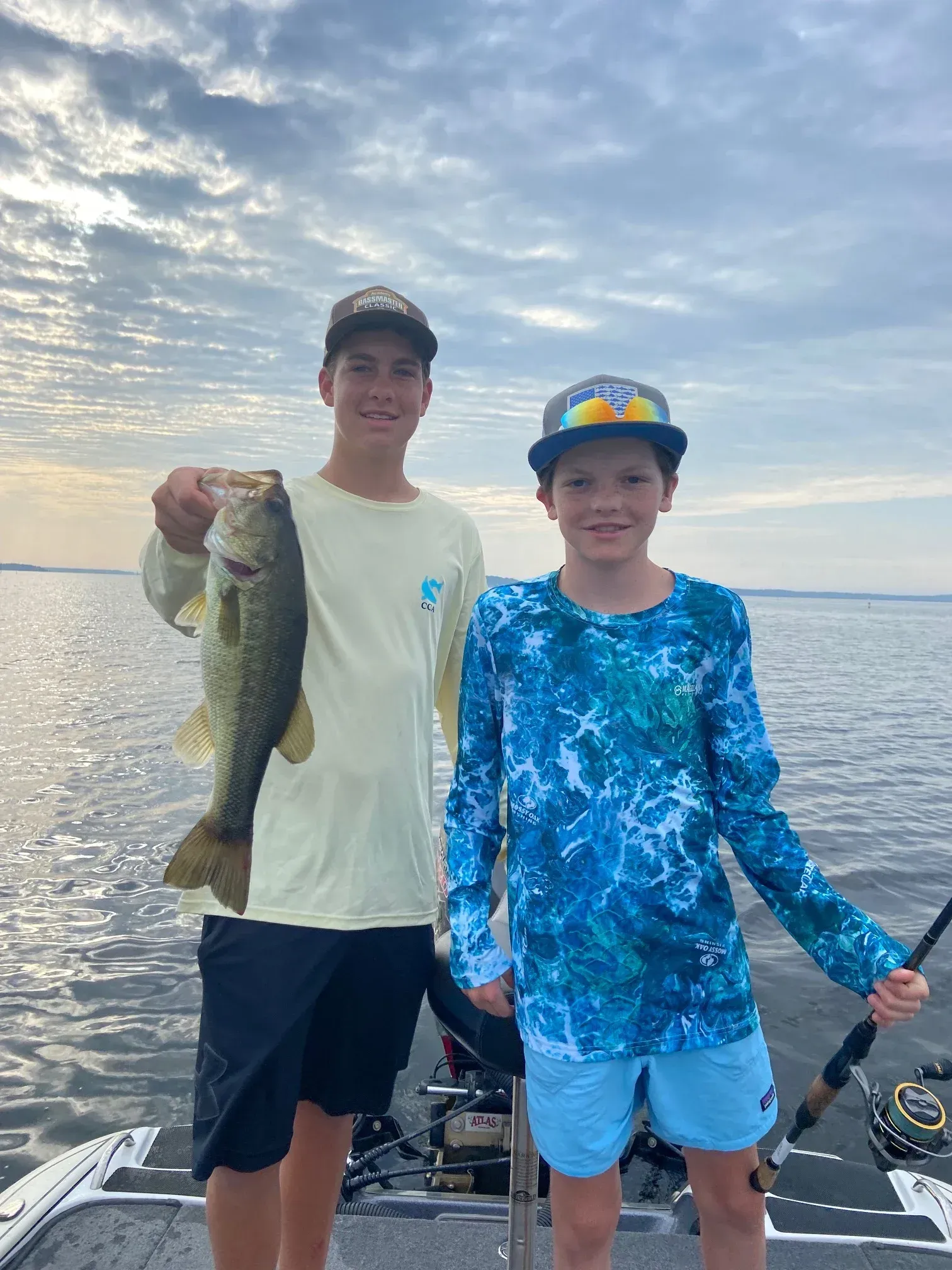 two young boys are standing on a boat holding a large bass .