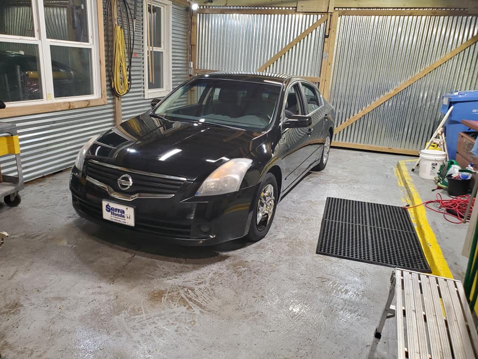 A black nissan altima is parked in a garage.