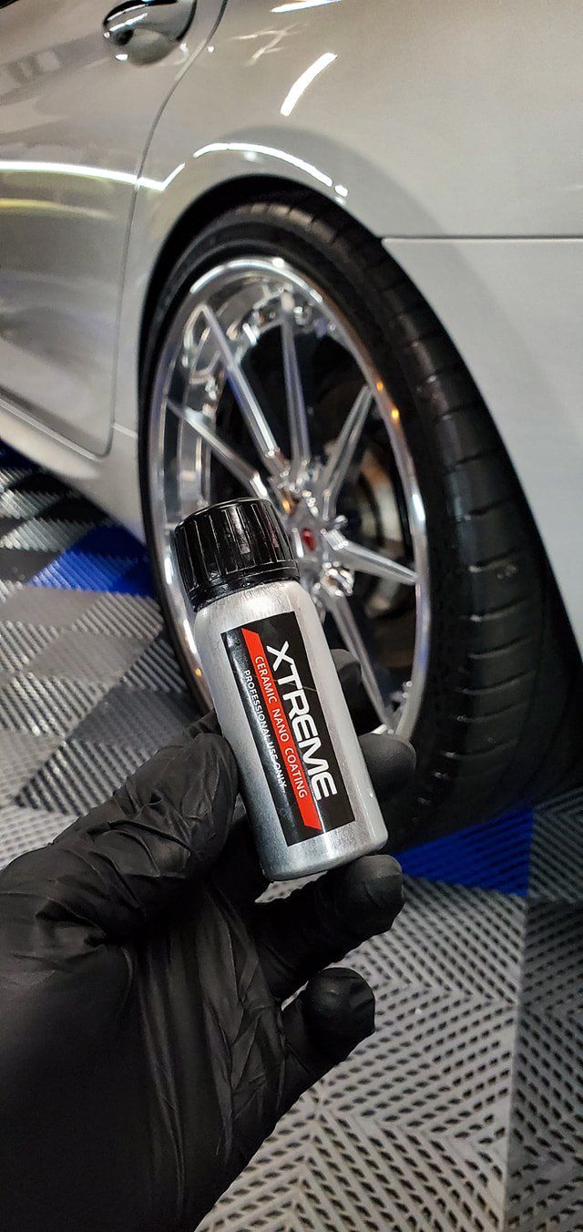 A person is holding a spray bottle in front of a car.