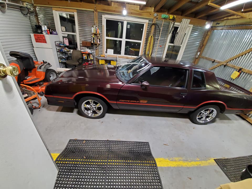A purple car is parked in a garage next to a lawn mower.