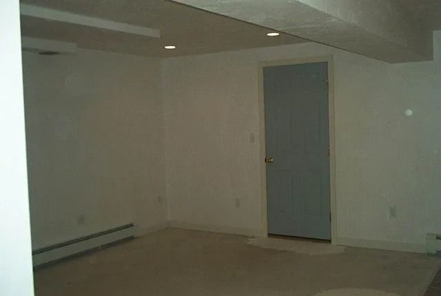 Empty room with beige walls, low ceiling, and a gray door in the back.