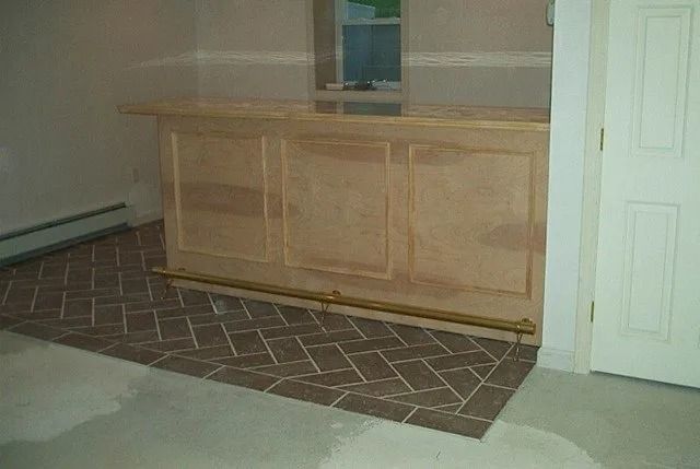Bare wooden cabinet against a wall with a patterned rug on the floor, beside a white door.