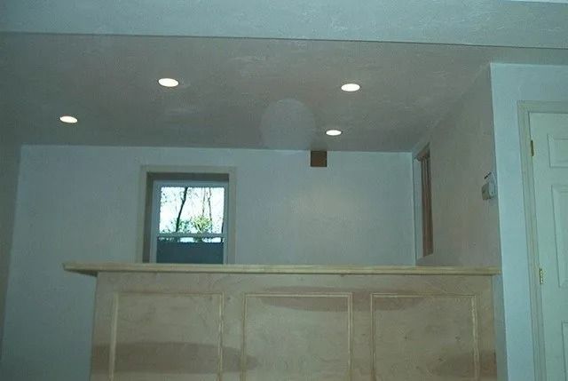 Empty room with a light wood bar counter, recessed ceiling lights, and a small window.