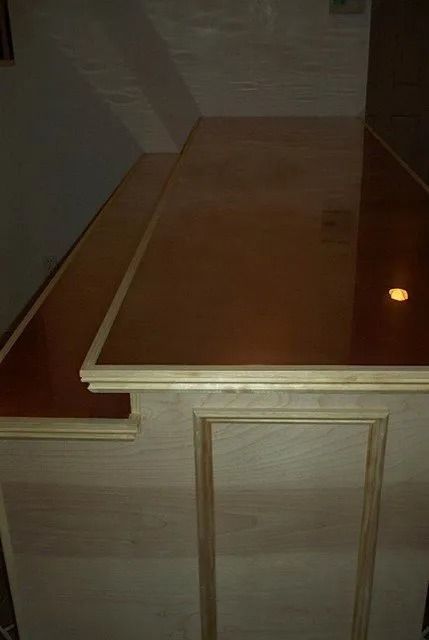Wooden cabinet or counter with a light brown top and cream paneled front in a dim room