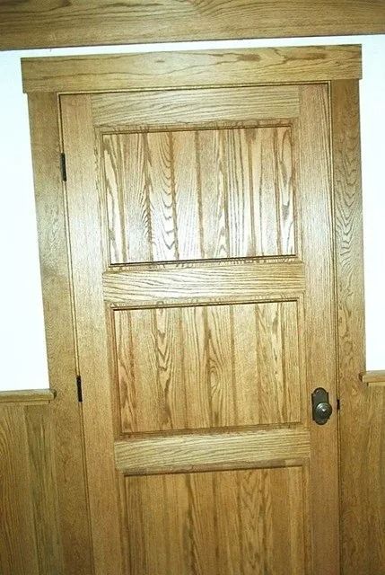 Wooden interior door with three panels and a dark knob, framed by white walls.