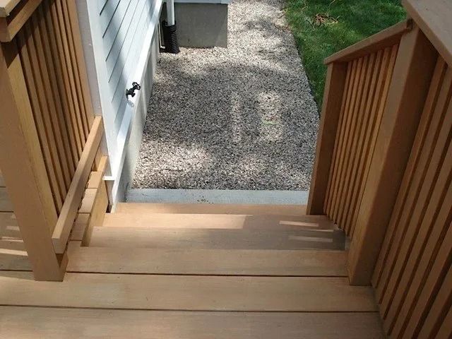 Wooden deck stairs leading down to a gravel path beside a house