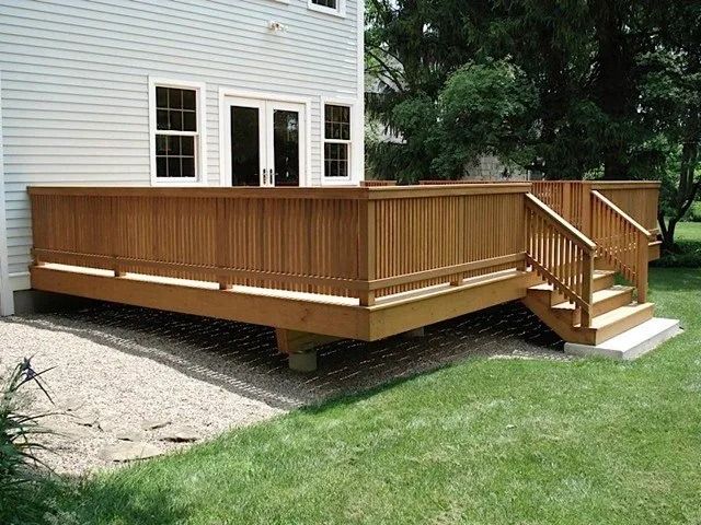 Wooden deck with railing and stairs attached to a house, beside a grassy yard.