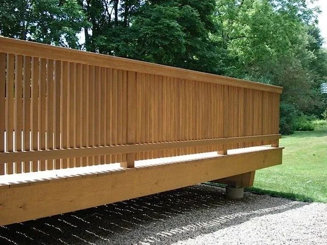 Wooden pedestrian bridge with vertical railings over a gravel path beside a grassy area