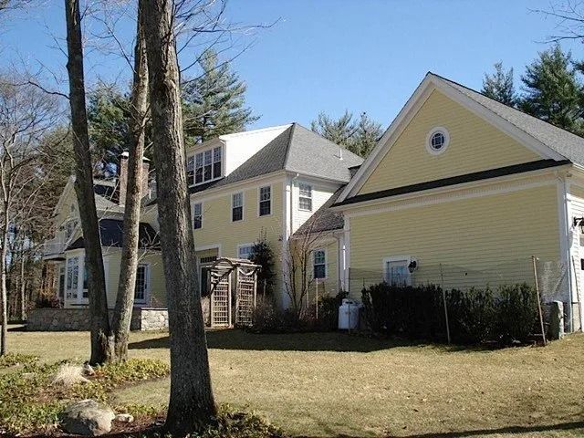 Yellow house with a side addition, trees, and a grassy yard on a sunny day