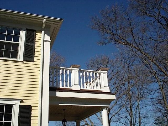Yellow house with white balcony and black shutters against a clear blue sky