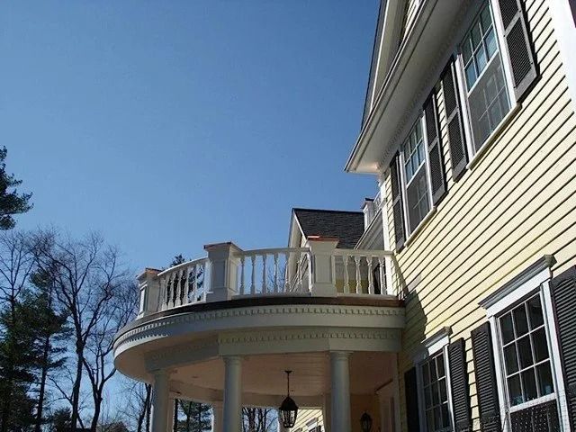 Yellow house with white trim and a curved second-story balcony against a blue sky