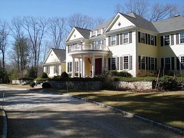 Large white suburban house with columns, a curved driveway, and bare trees in front