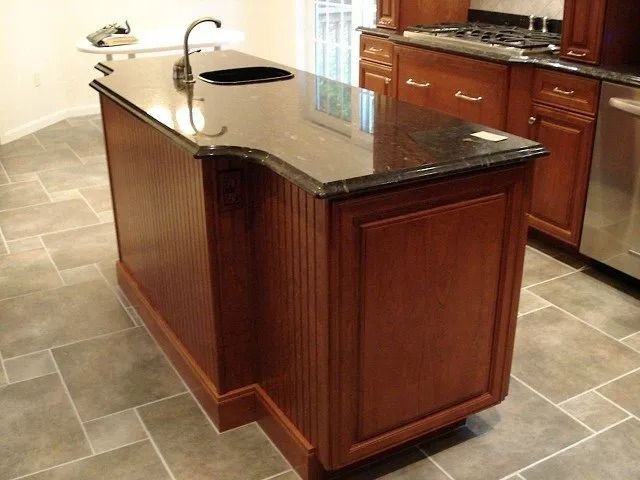 Wood kitchen island with dark granite countertop and built-in sink in a tiled kitchen.