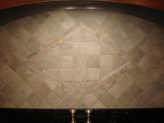 Decorative tiled fireplace wall with a diamond-patterned center and two metal fireplace tools below