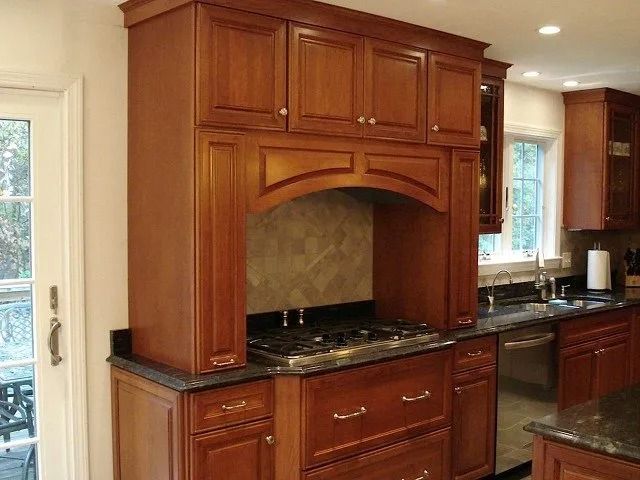 Wooden kitchen cabinetry framing a granite countertop and built-in stove under a hood alcove