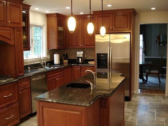 Modern kitchen with wooden cabinets, granite island, stainless steel refrigerator, and pendant lights