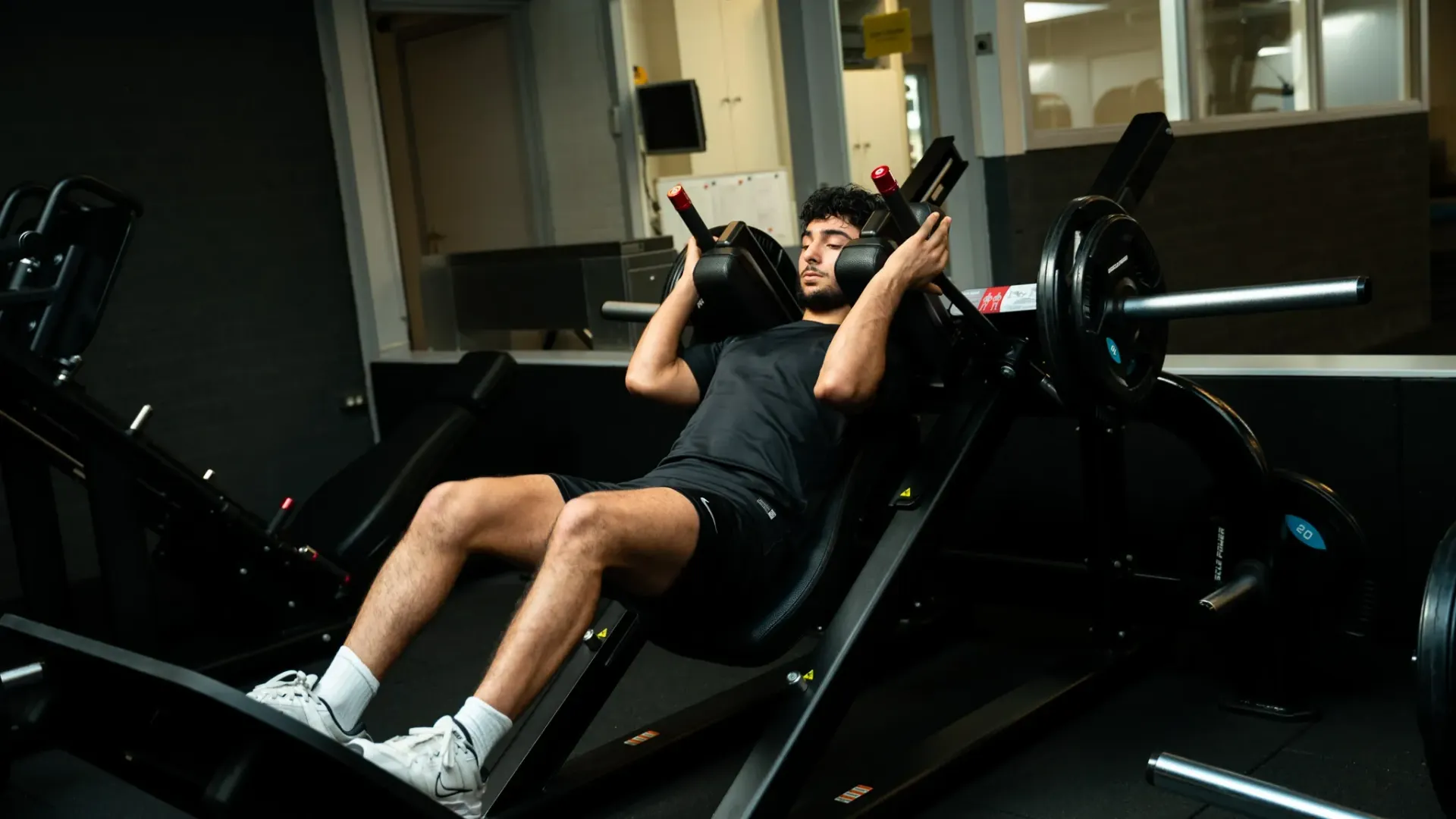Een man zit op een hack squat machine in een sportschool.