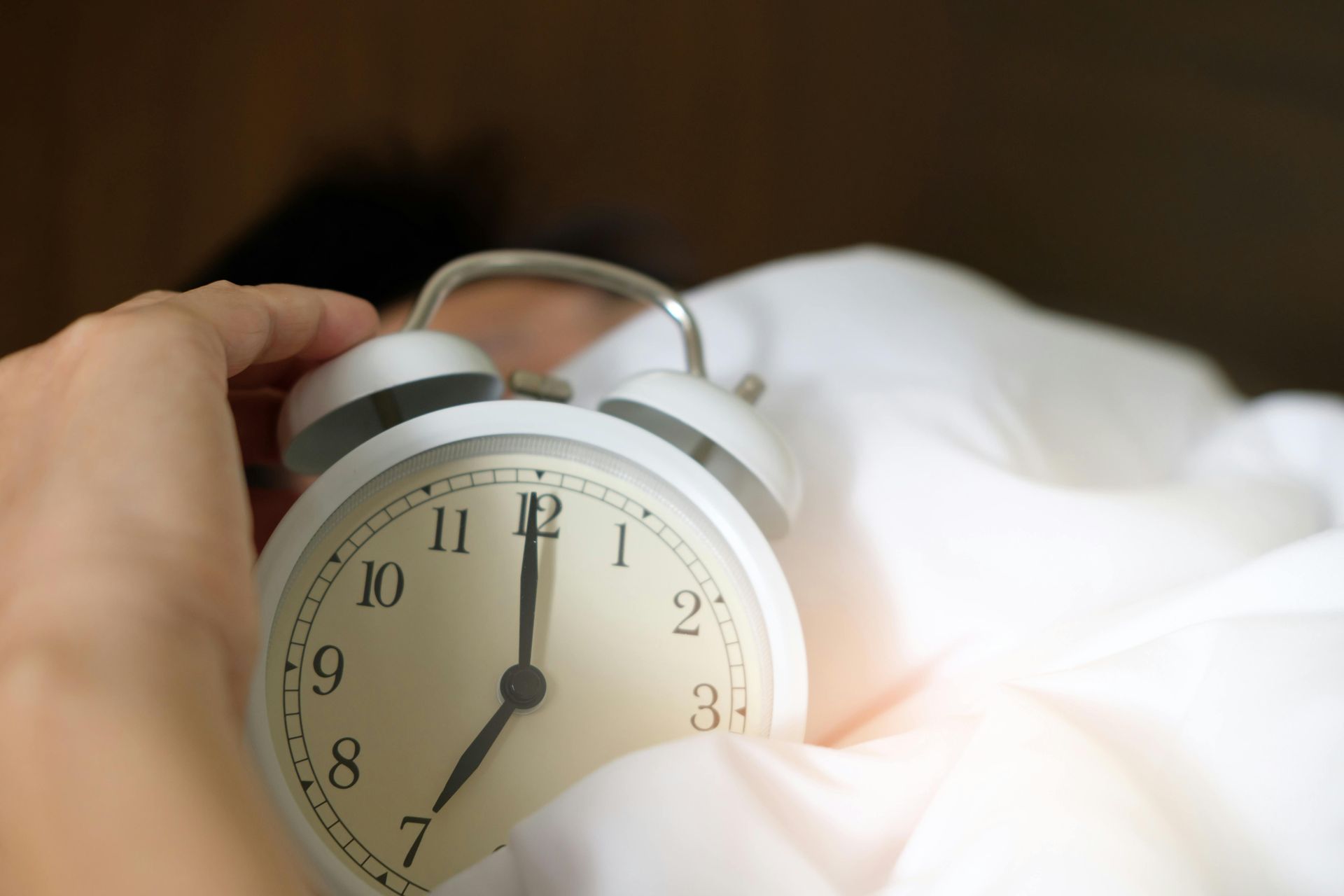 Iemand houdt een wekker in zijn hand terwijl hij in bed ligt.