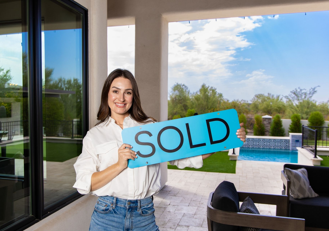 A smiling person holding a bright blue sign that says 