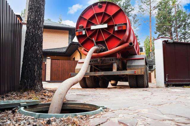 A septic tank pumping truck servicing a tank in a residential area.