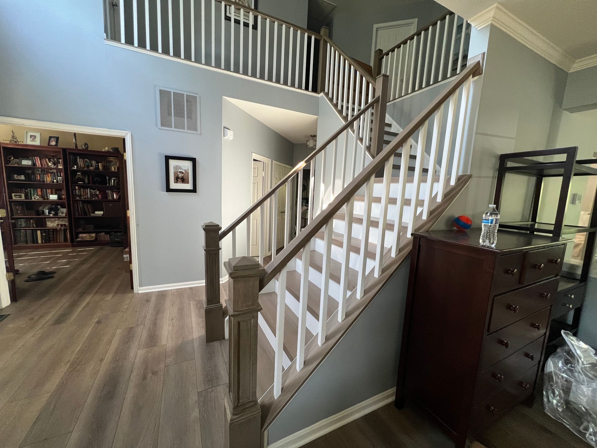 A staircase in a house with a wooden railing and a dresser.