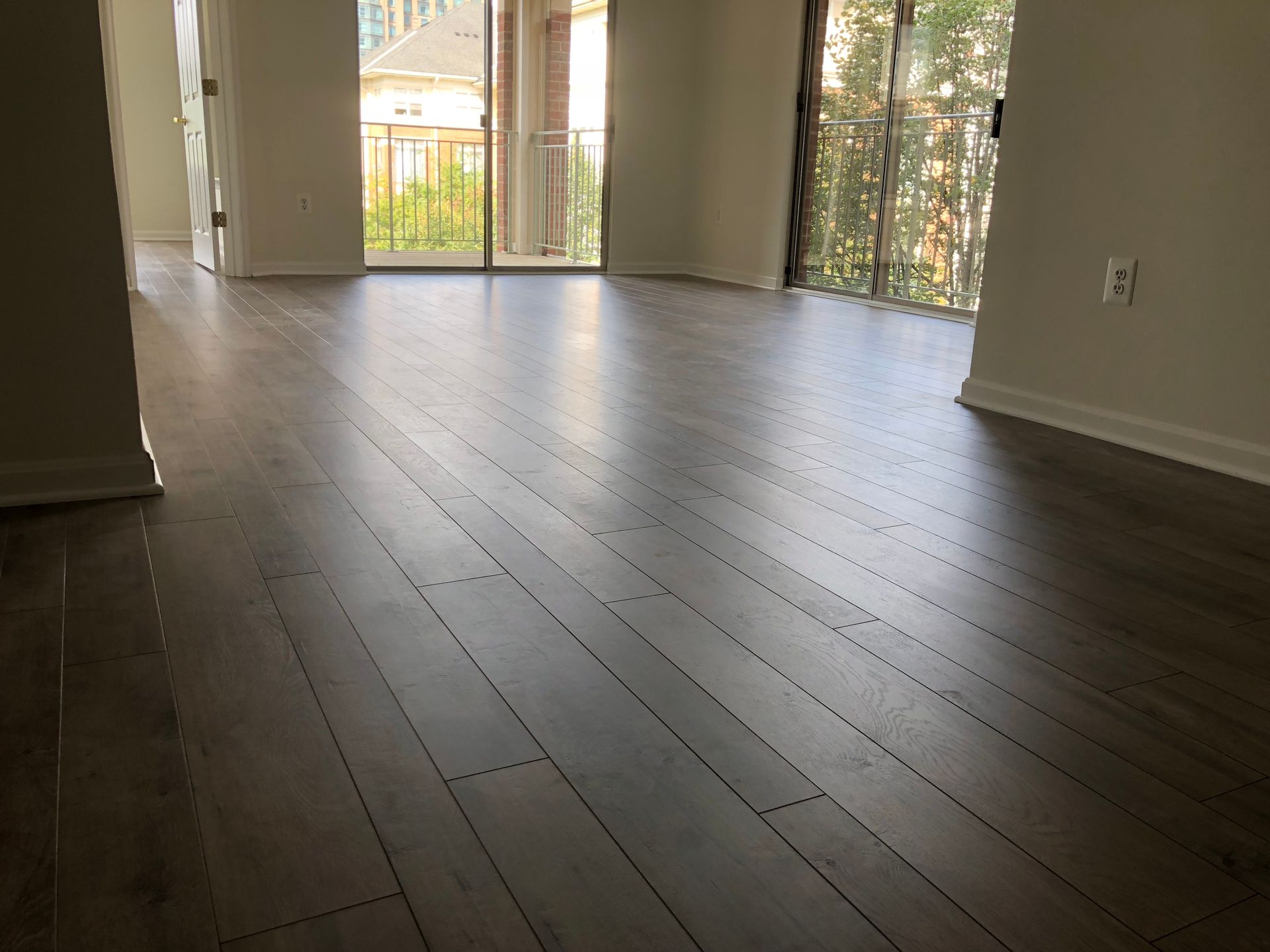 An empty living room with hardwood floors and sliding glass doors.