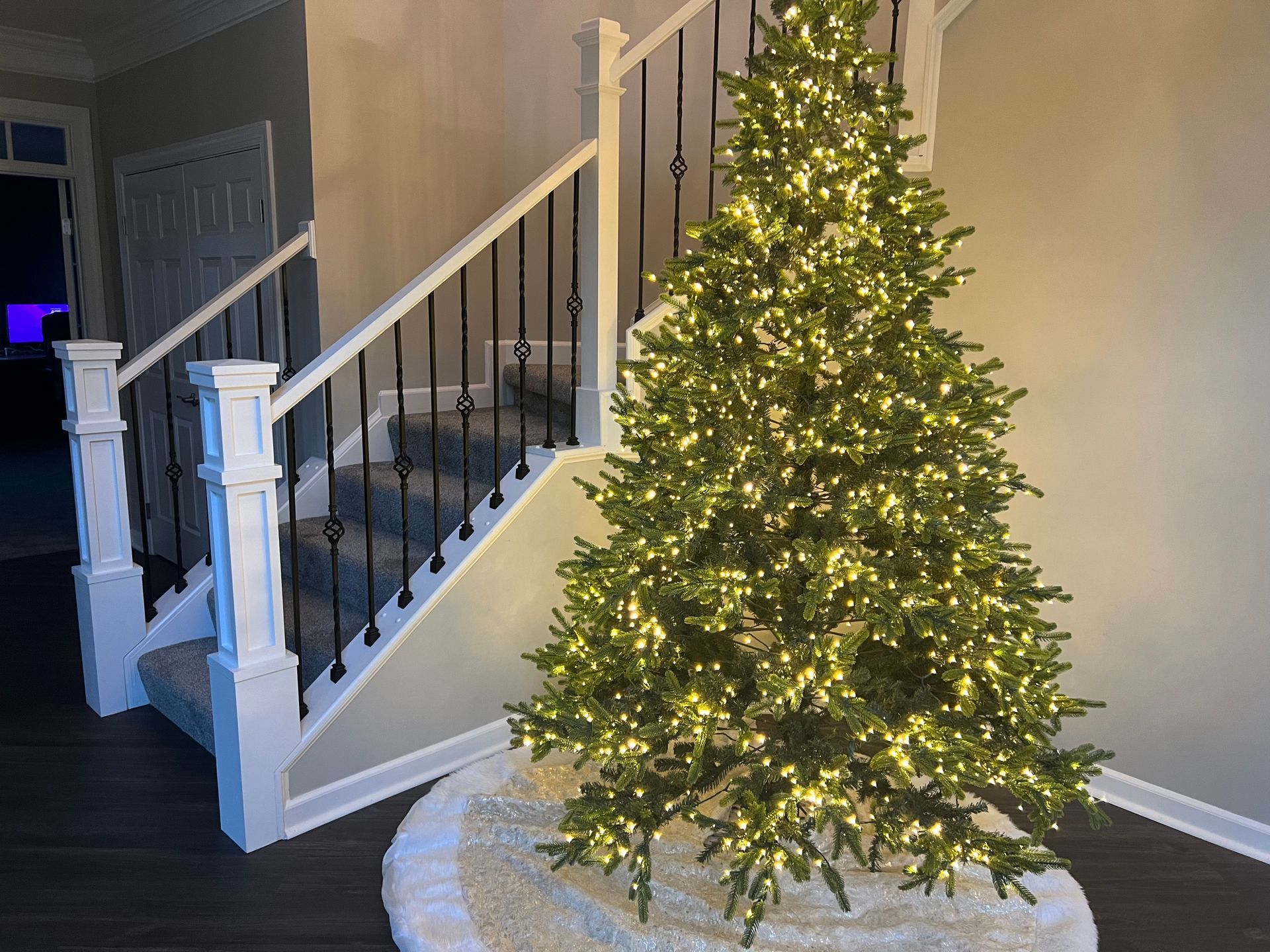 A christmas tree is sitting in front of a staircase in a living room.