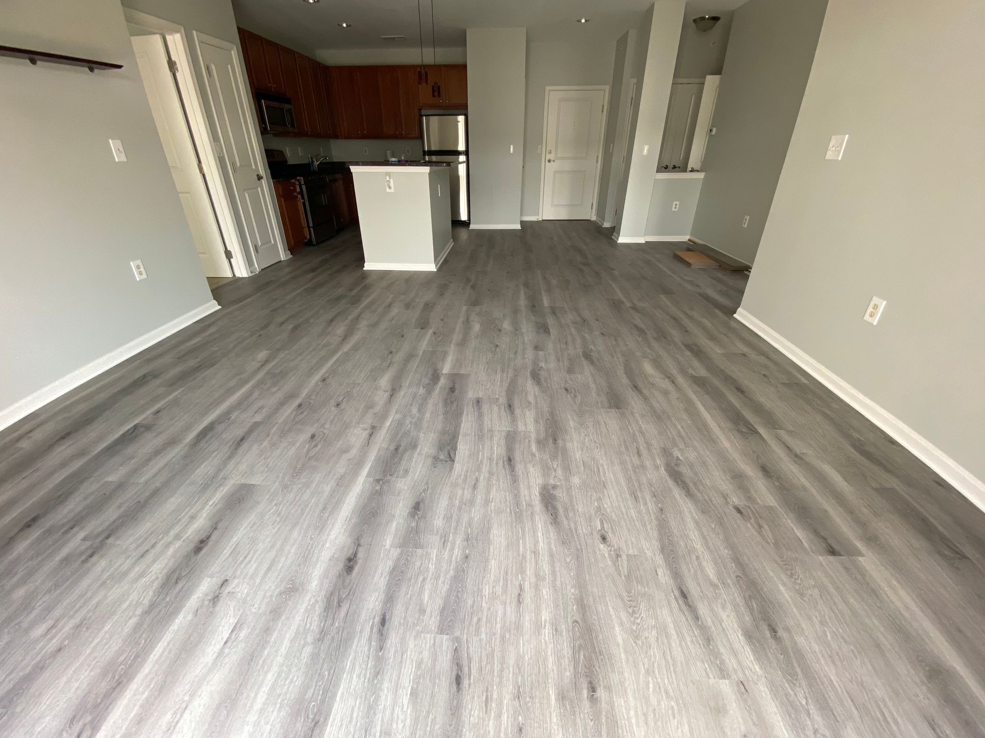 A living room with hardwood floors and a kitchen in the background.