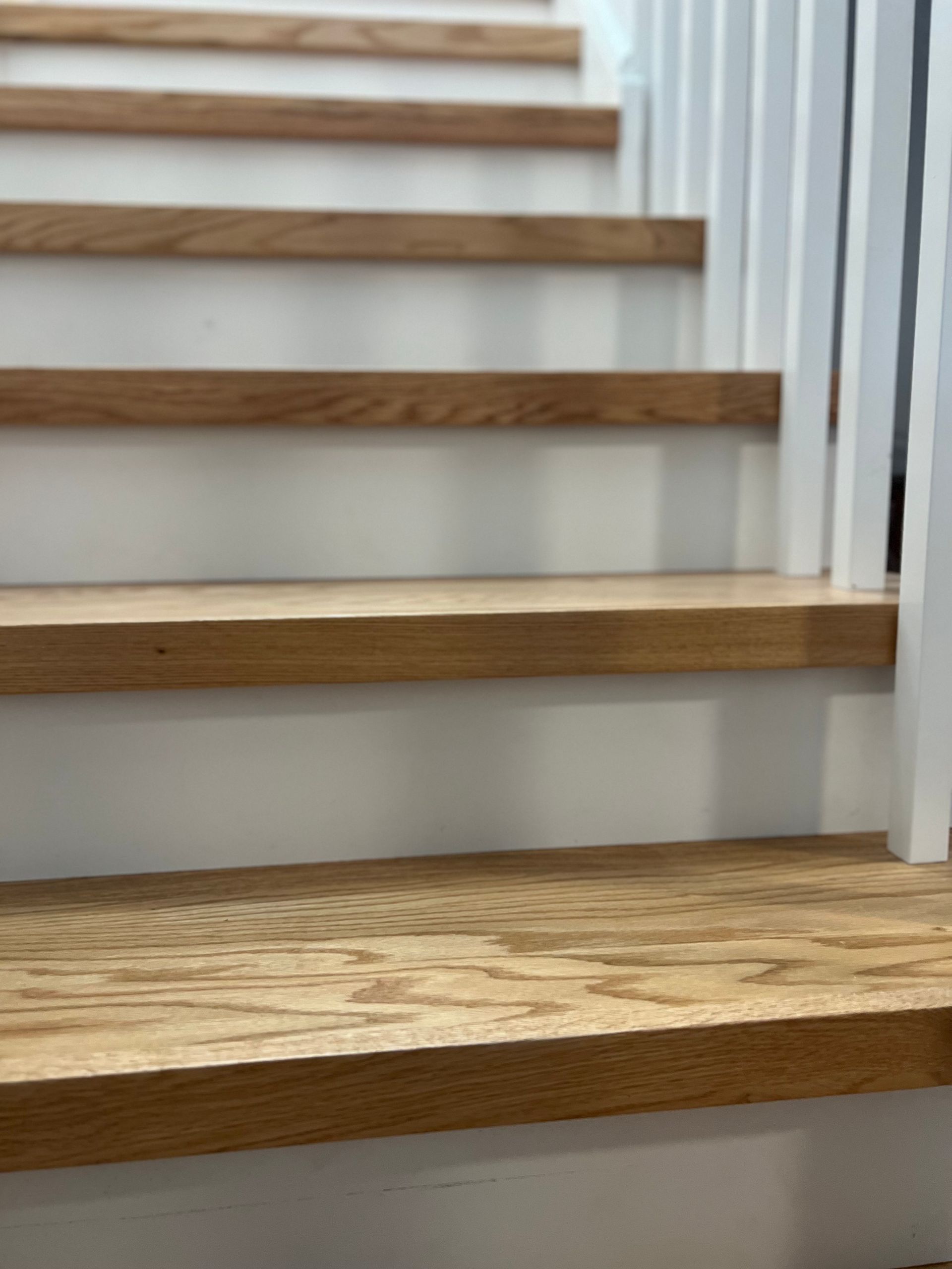 A close up of a set of stairs with wooden steps and a white railing.