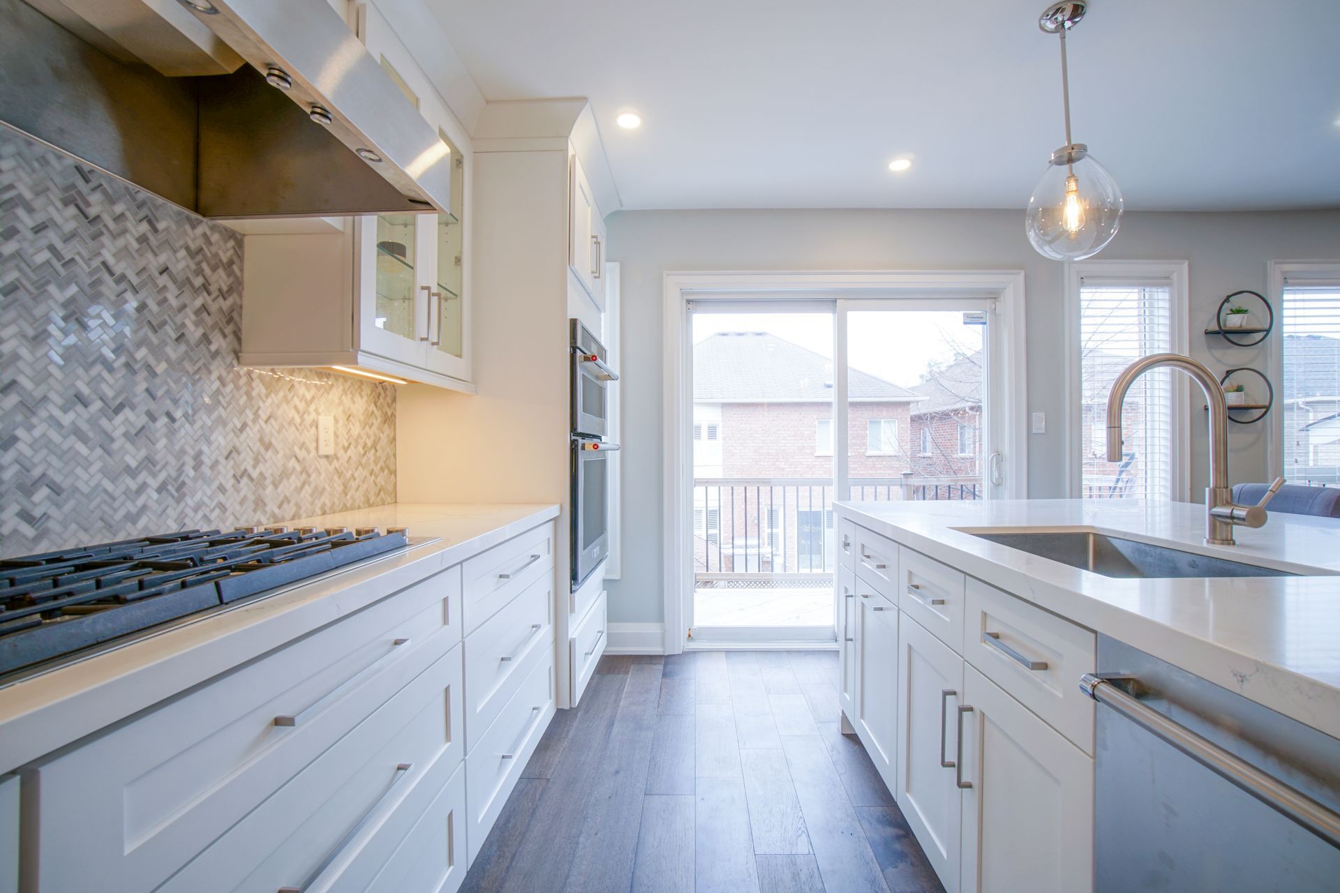A kitchen with white cabinets , a stove top oven , a sink , and a sliding glass door.