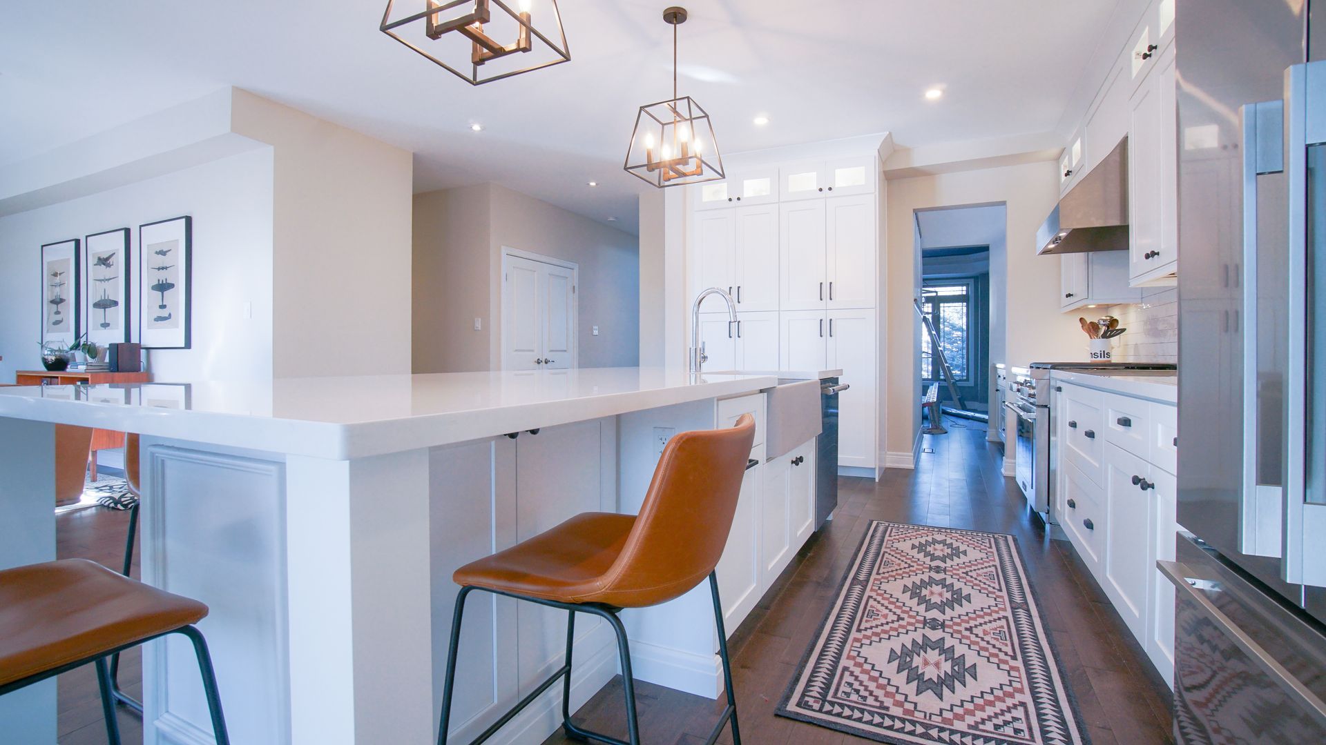 A kitchen with white cabinets , stainless steel appliances , a rug and a chair.