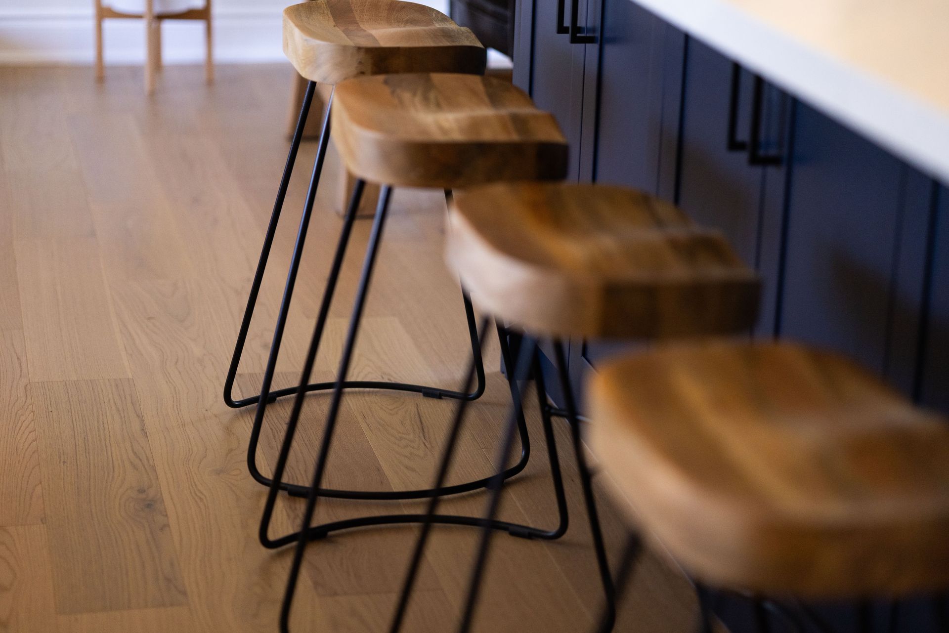A row of wooden bar stools are sitting next to each other in a kitchen.