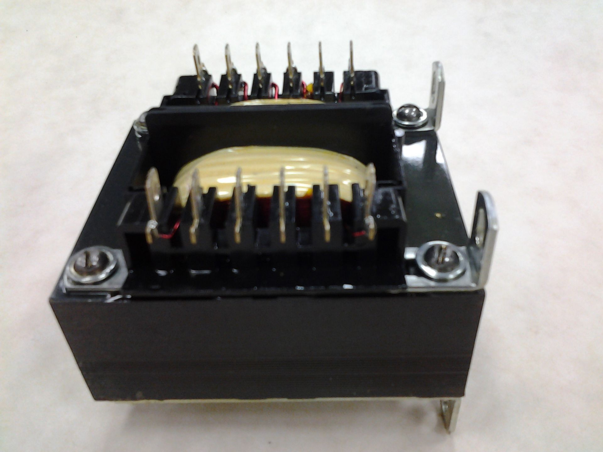 A black transformer with multiple pin connectors, mounted on a white surface