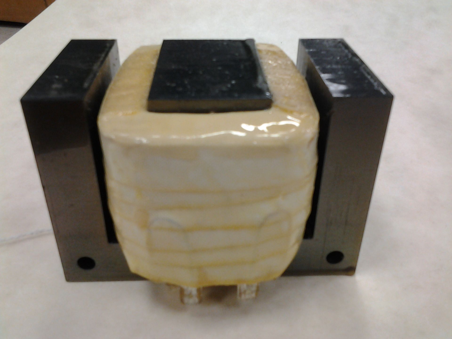 A transformer with a beige-wrapped coil and black metal core, sitting on a surface